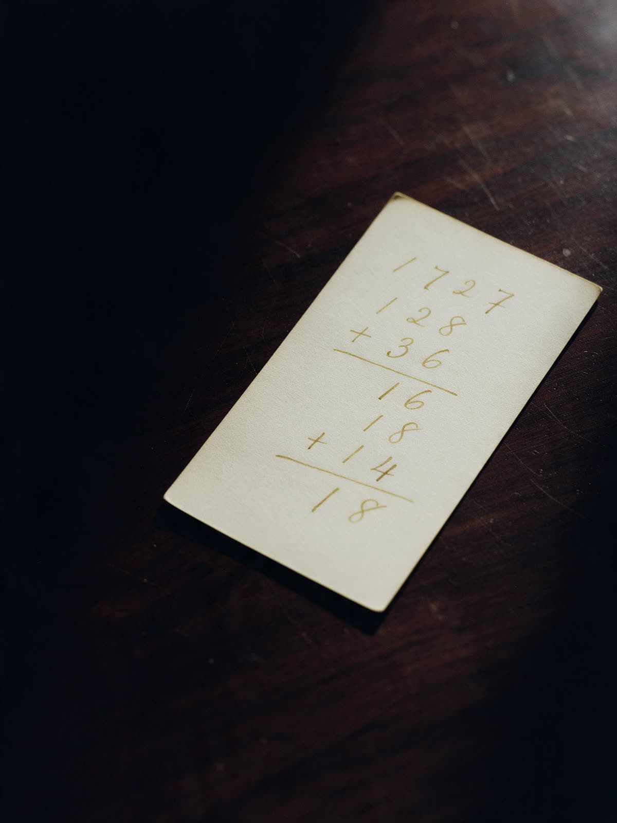 Una ficha de papel con una fecha descompuesta en cifras y sumada a mano en tinta dorada, sobre una mesa de madera oscura.
